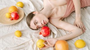 A serene woman in pink lies among vibrant citrus fruits on a soft linen cloth.